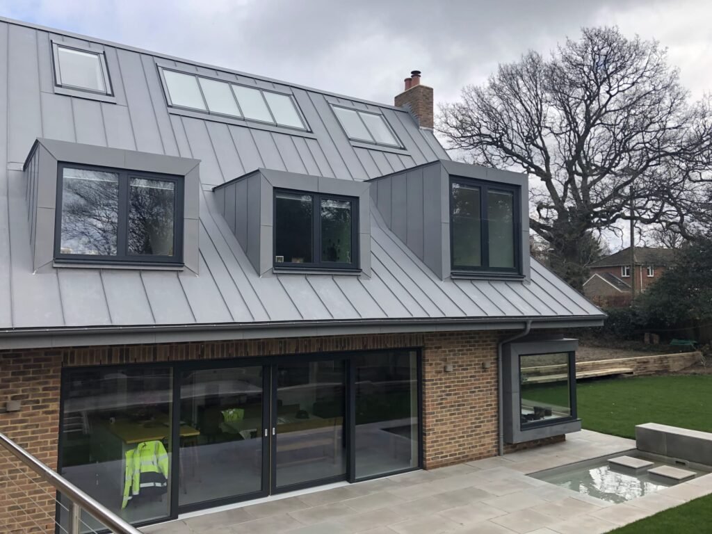 Modern residential home with a grey zinc-clad mansard roof extension and large glass sliding doors.